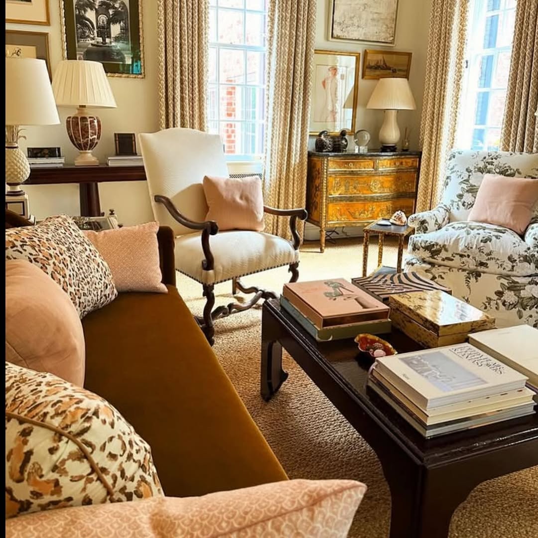 A traditional living room with chic dark brown sofas, an armchair, wooden coffee table with books, lamps, framed art, and large windows with drapes—perfect for gathering inspiring living room ideas.