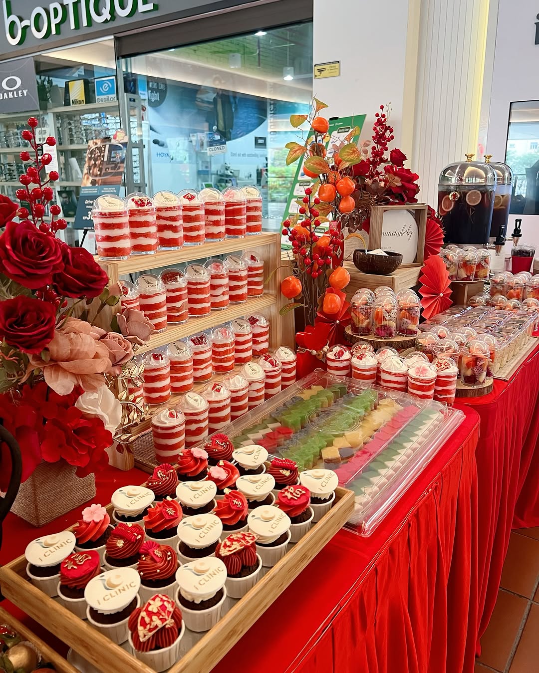 A dessert table with party desserts like cupcakes, layered parfaits, macarons, and assorted sweets on red tablecloths, decorated with red flowers and festive ornaments—perfect for memorable desserts and creative dessert table ideas.