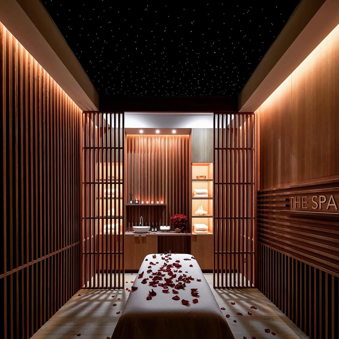 A serene massage room with wooden paneling, a massage table covered in rose petals, shelves with towels and decor, and star-like ceiling lights—perfect inspiration for your next massage room ideas.