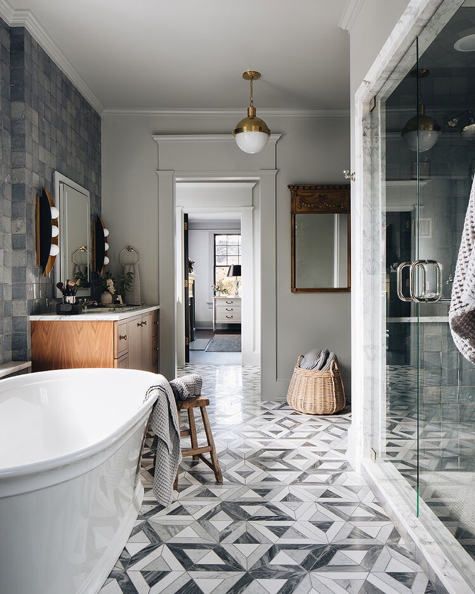 Modern bathroom design with geometric tile floor, freestanding tub, glass shower, wooden vanity, round mirror, woven basket, and a view into an adjoining room—perfect inspiration for fresh bathroom tile ideas.