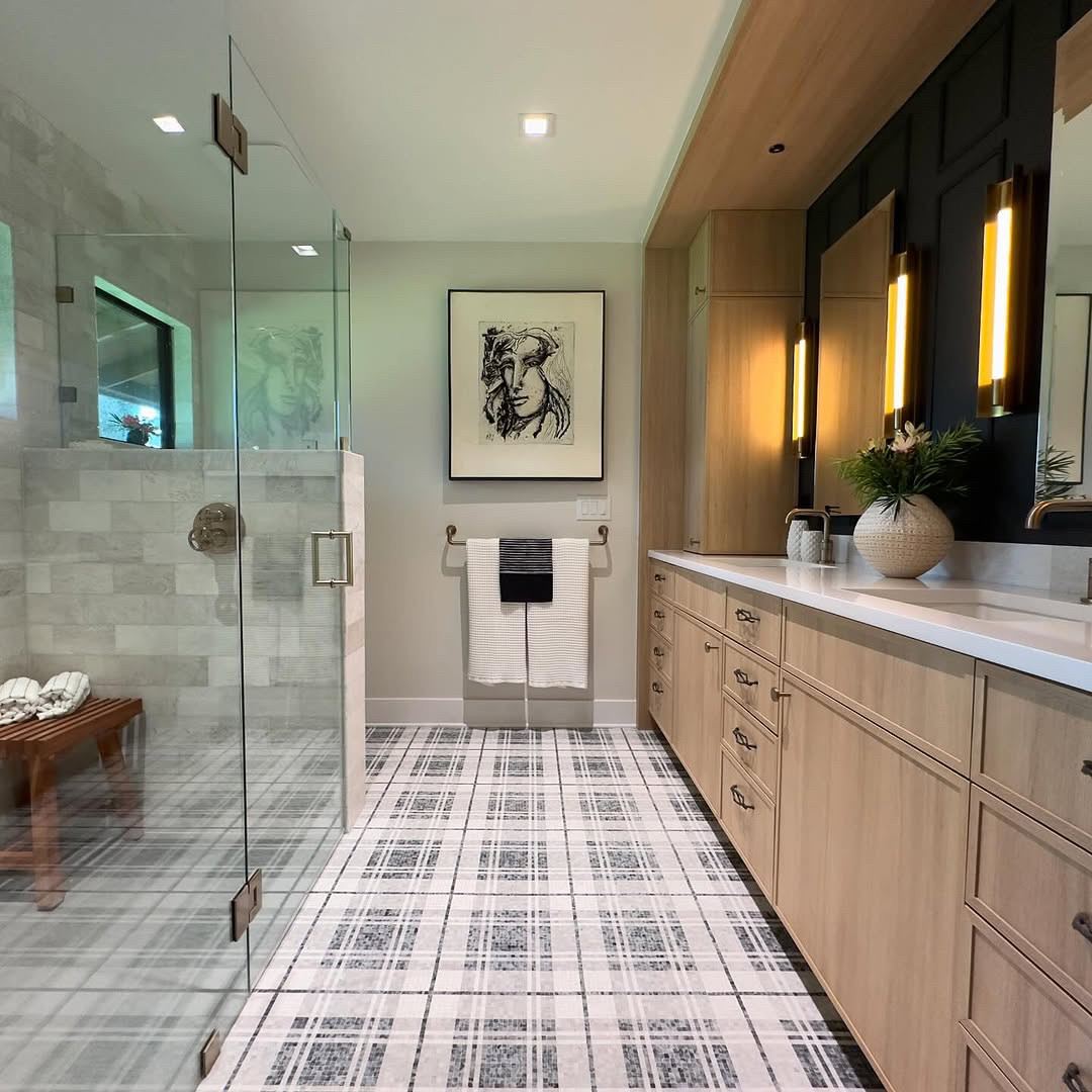 Modern bathroom design with glass shower, wood cabinets, plaid tile floor showcasing fresh bathroom tile ideas, wall art above the towel rack, and illuminated mirrors for a spa-worthy bathroom feel.