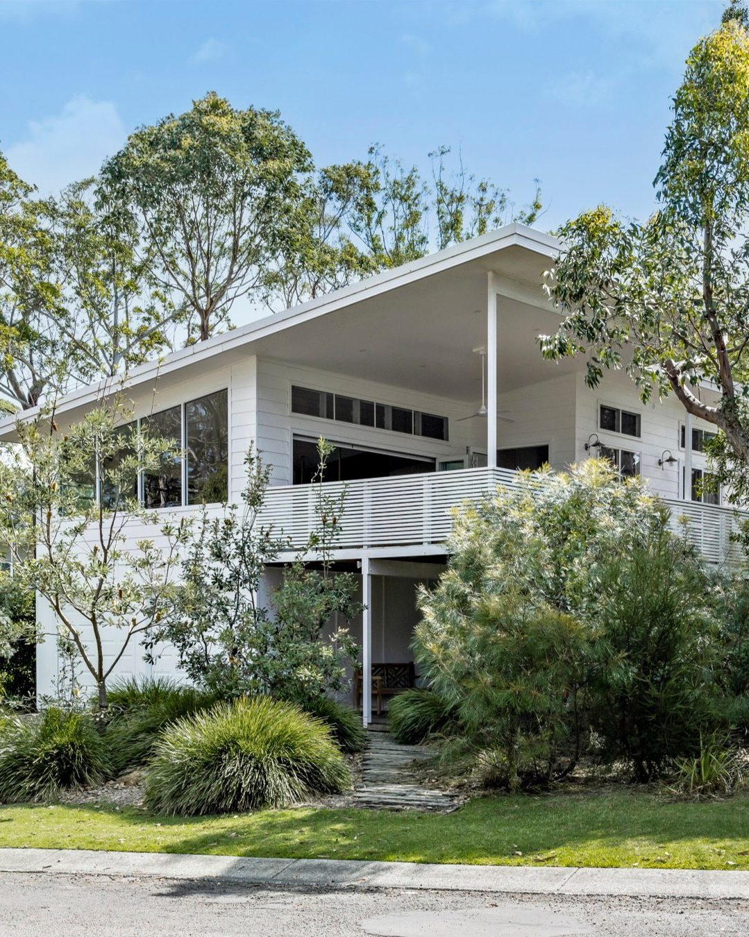 Ultra-stylish modern two-story white house with large windows and a wraparound balcony, surrounded by trees and shrubs on a sunny day—perfect inspiration for design ideas 2025.