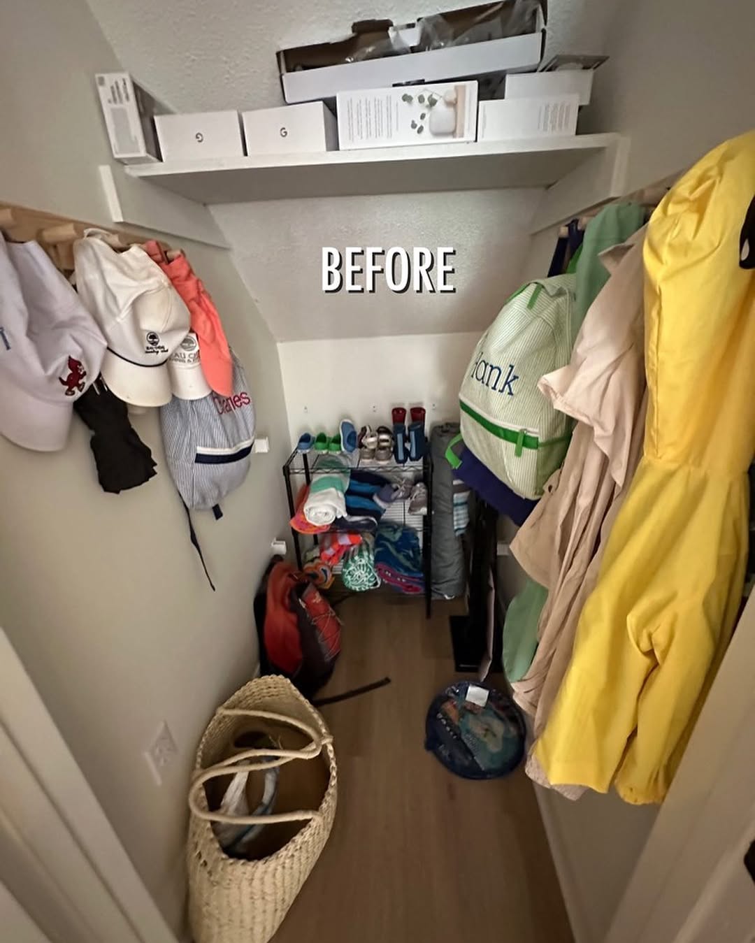 A small under the stairs closet with hats hanging on the left, jackets on the right, and various bags and items stacked on the floor; the word