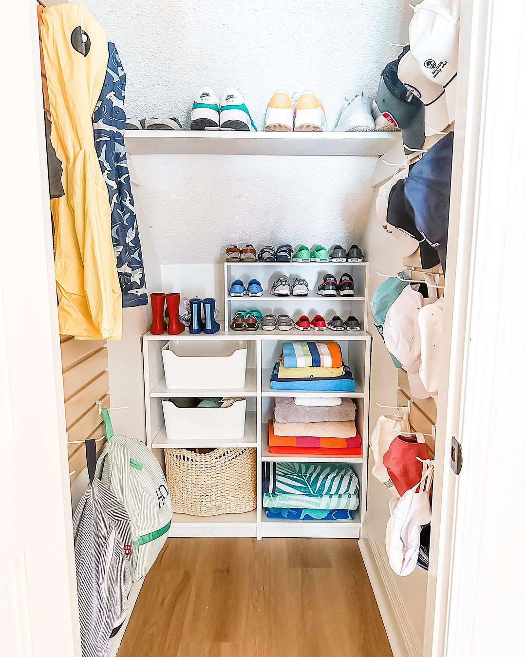 A neatly organized under stairs closet with clothes, hats, shoes, towels, and accessories arranged on shelves, hangers, and hooks. The floor is clear and the space is tidy—a great example of clever under stairs storage.
