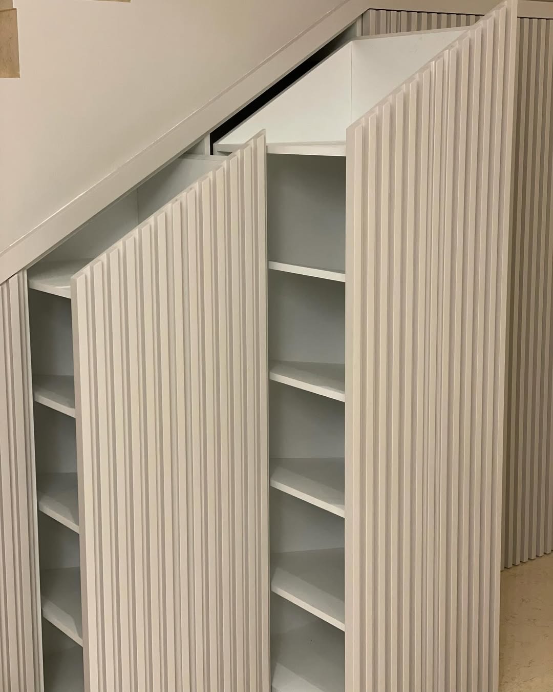 Three pull-out storage cabinets with vertical grooves are built into the space beneath a staircase, offering clever Under Stairs Storage with multiple shelves—an inspiring addition to modern Closet Ideas.
