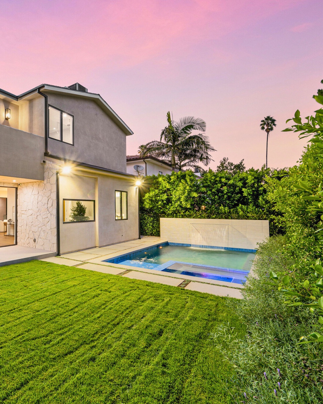 Modern backyard with green lawn, a small rectangular pool with built-in spa, water feature, and privacy hedges at sunset—perfect for those seeking cool pool ideas or inspiration for stylish backyard pools.