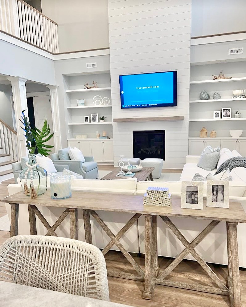 Modern living room with white sofas, light wood furniture, wall-mounted TV, built-in shelves living room accents, decorative items, and a fireplace beneath the TV.