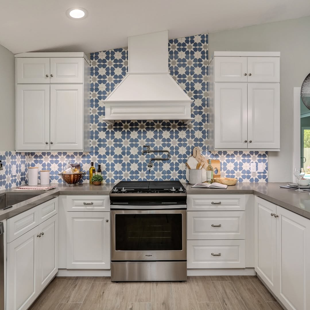 Modern kitchen with white cabinets, stainless steel stove, patterned blue and white tile backsplash, and light wood flooring—showcasing stunning kitchen colors inspired by upcoming kitchen color trends 2025.