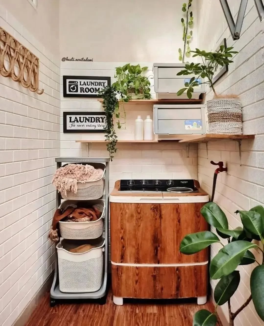 A compact Boho laundry room featuring a wooden washing unit, laundry baskets, white tiled walls, and wall shelves adorned with plants and storage boxes—perfect for those seeking relaxed boho laundry decor.