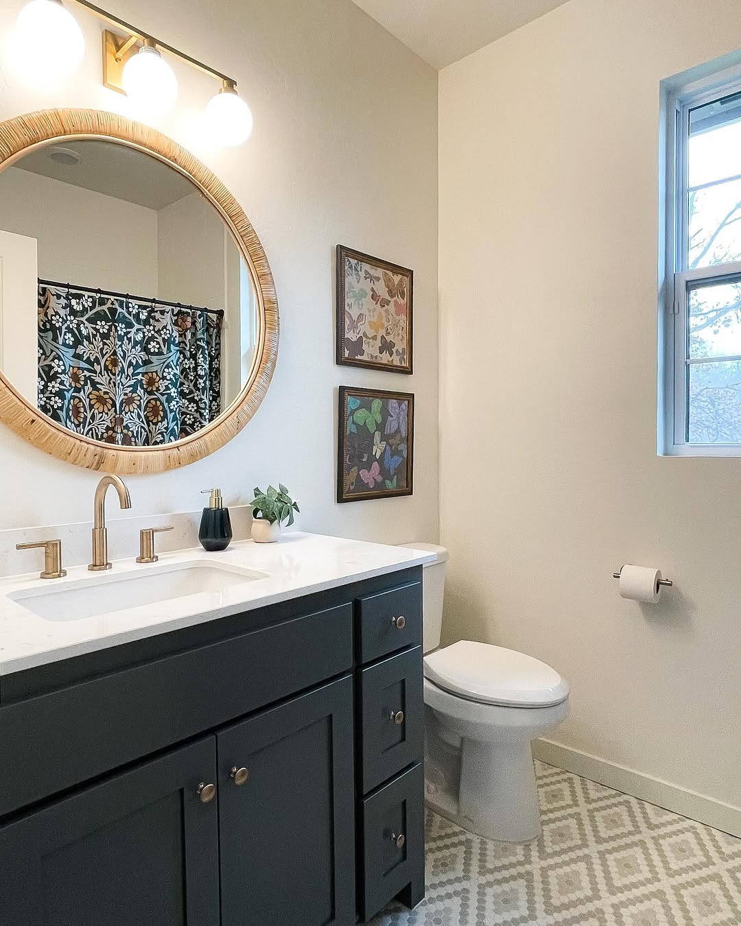 A modern kids bathroom with a round mirror above a black vanity, two framed pictures on the wall, a toilet, and a window letting in natural light.