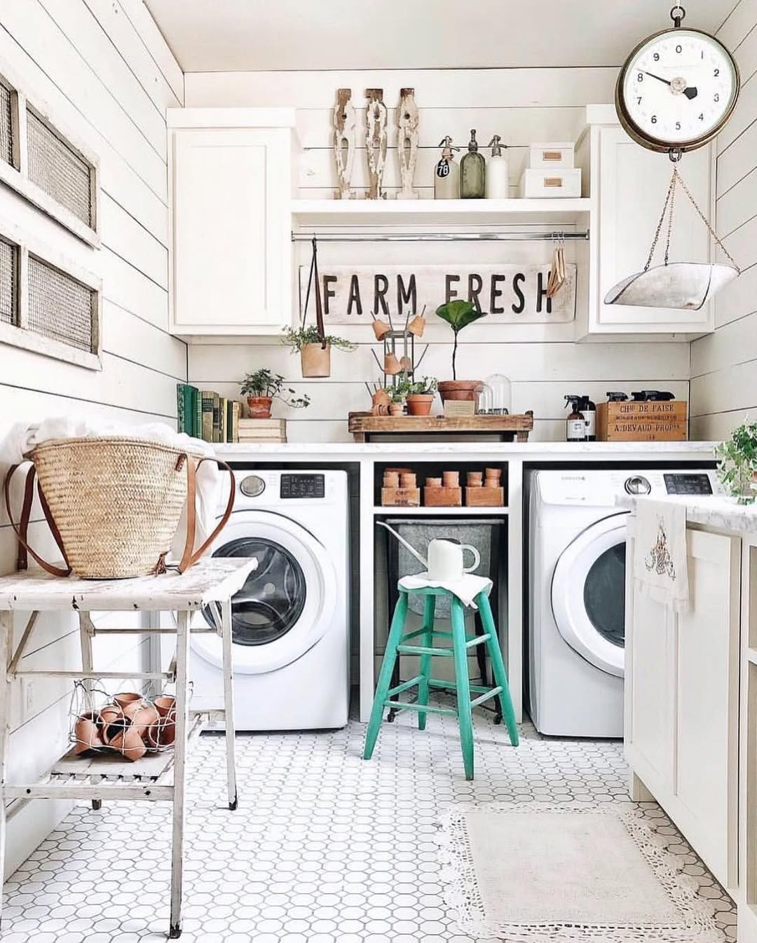 A bright, farmhouse-style laundry room with white shiplap walls, boho decor accents, a washer and dryer, potted plants, rustic touches, and a green stool in front of a shelf labeled