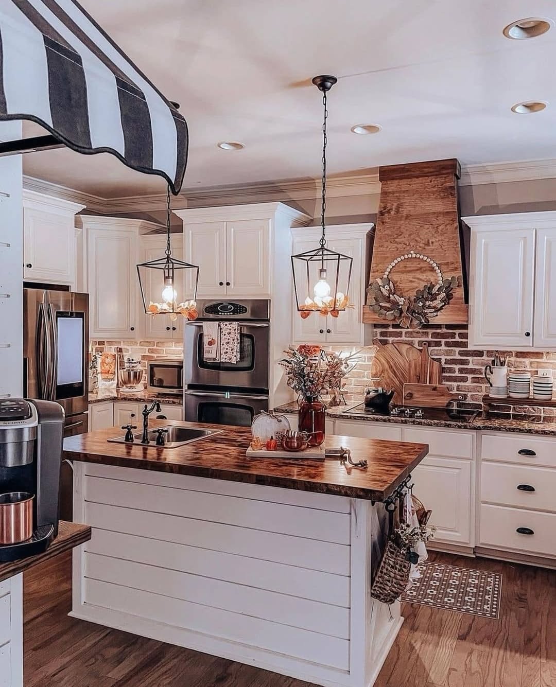 A farmhouse kitchen featuring white cabinets, a wood-topped island, stainless steel appliances, pendant lighting, brick accents, and charming farmhouse decor—perfect for inspiring your next kitchen ideas.