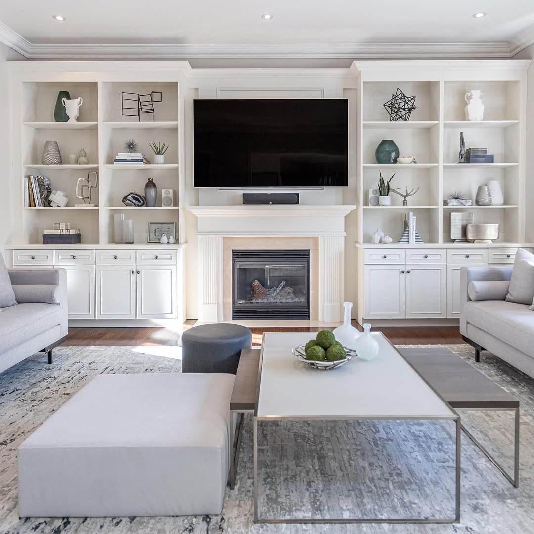 Contemporary built-in shelves living room featuring a fireplace, wall-mounted TV, neutral-toned furniture, and decorative accents atop a patterned rug.