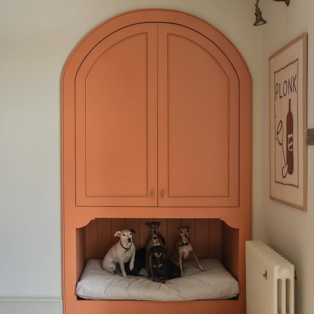 Four small dogs sit together on a cushioned alcove bed built into a peach-colored cabinet, showcasing stylish pet furniture and pet room decor, with a