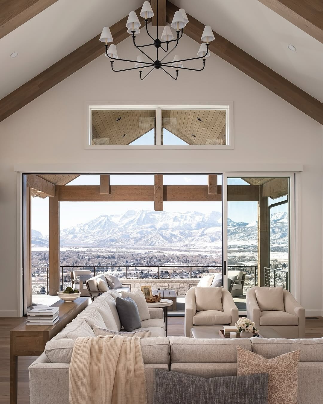 Spacious organic modern living room with vaulted ceiling, modern chandelier, neutral furniture, and large sliding doors opening to a patio with stunning mountain views.