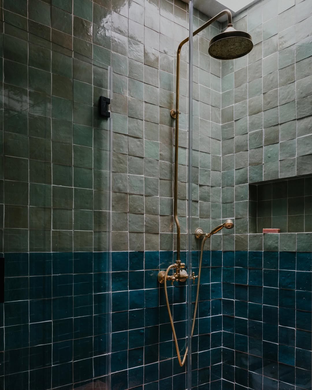 A shower area with green and dark teal square bathroom tiles, a gold shower fixture, rainfall showerhead, and a built-in wall niche—perfect for those seeking inspiring bathroom tile ideas and a spa bathroom feel.