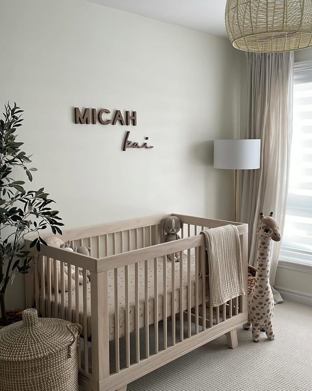 A minimal nursery with a light wood crib, plush giraffe toy, neutral bedding, floor lamp, and