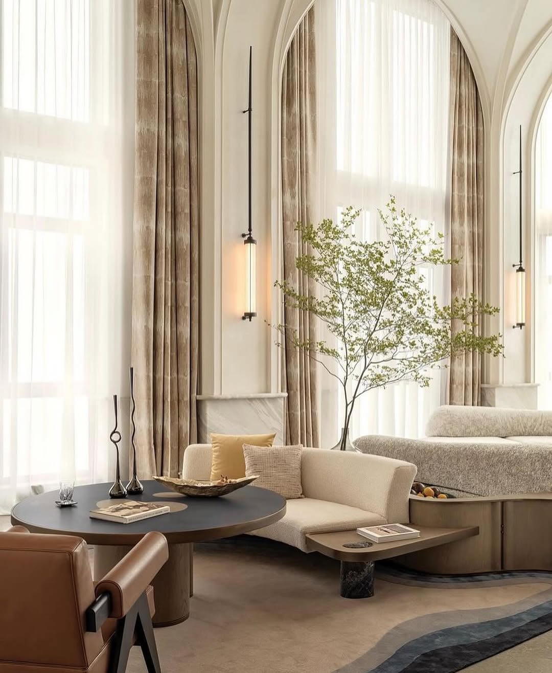Modern living room featuring arched windows, sheer curtains, neutral-toned furniture, a round black table, decorative vases, and a potted green plant near a curved sofa—perfect for fresh organic modern living room inspiration.