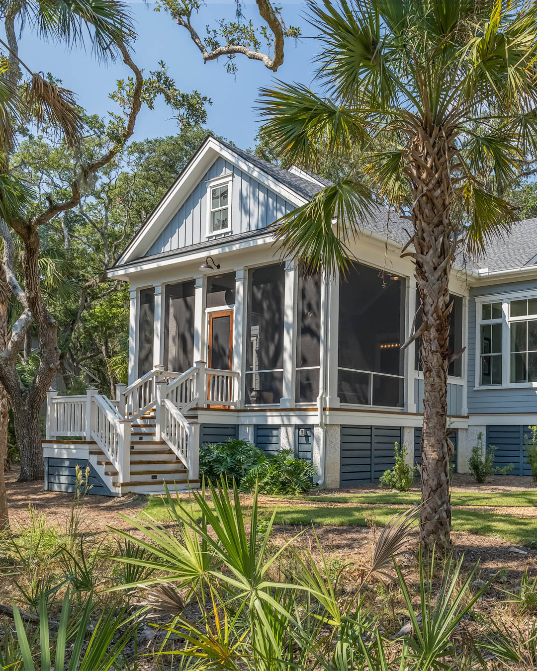 A light blue house with a screened-in porch, white trim, and steps leading to the front door, surrounded by palm trees and greenery—perfect inspiration for coastal cottage exterior style.