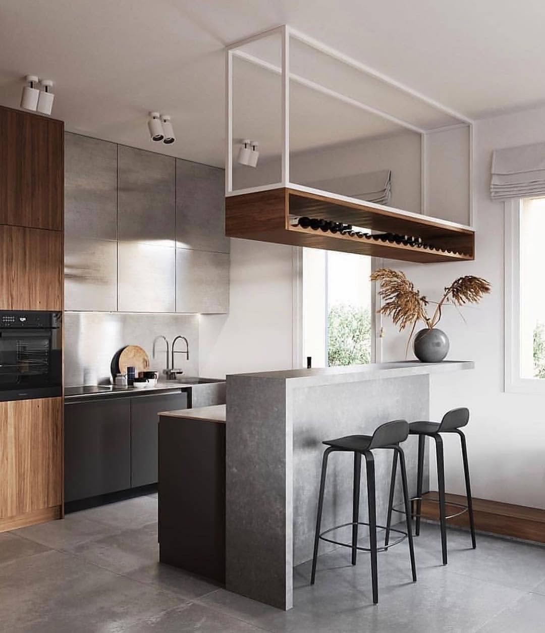 Modern kitchen with wood and gray cabinetry, a minimalist breakfast bar with two black stools, overhead wine storage, and a vase with dried branches on the counter—perfect for showcasing stylish wine rack ideas.