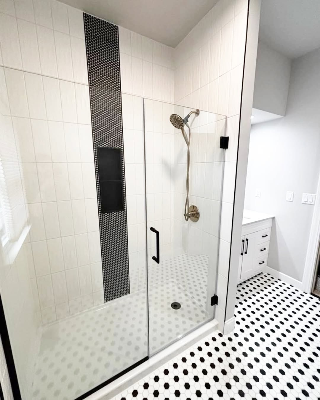 Modern bathroom design with a glass-enclosed shower featuring white tiles, a black vertical accent strip, and a black-and-white hexagonal tile floor—offering inspiring bathroom tile ideas.