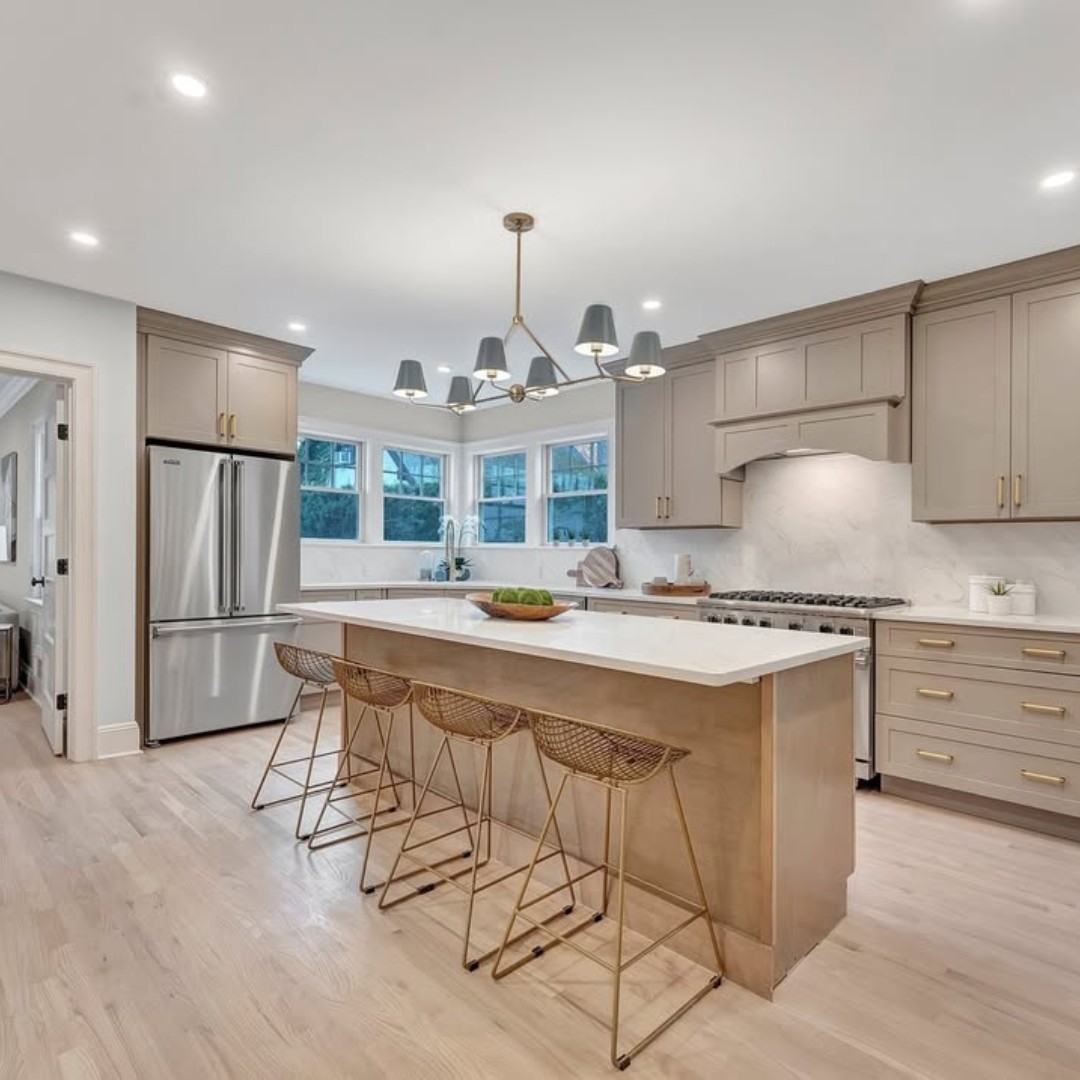 Modern kitchen with light wood floors, beige cabinets, and stainless steel appliances. A central island with bar stools and a contemporary chandelier showcase one of the stunning kitchens featuring top kitchen color ideas for 2025.