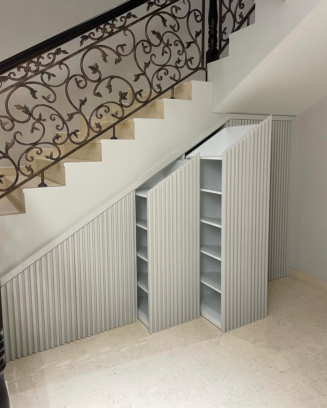 Built-in shelves with vertical grooves are installed under a staircase, providing clever storage under stairs and making the most of the triangular space created by the steps above.