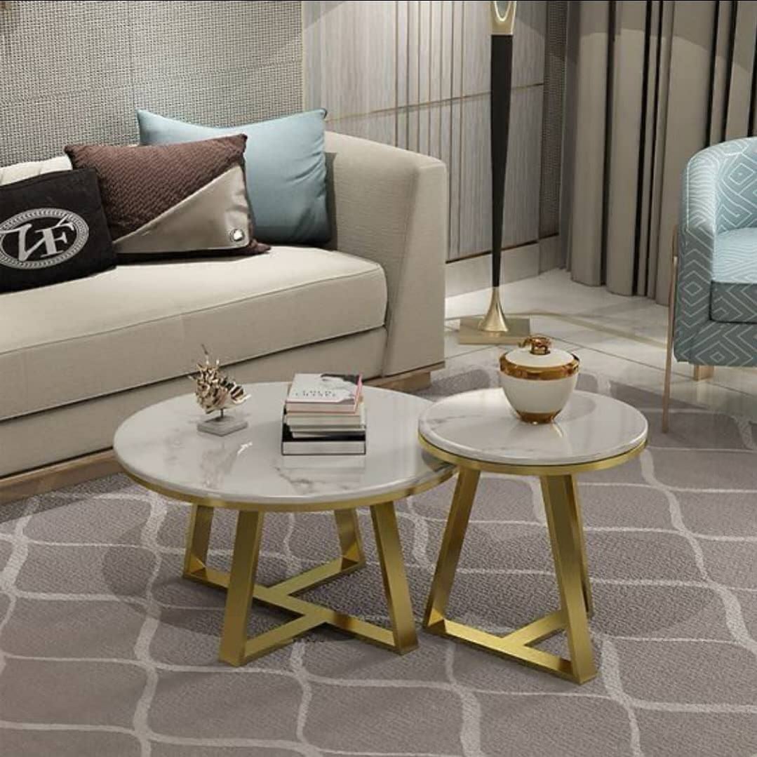 Two round marble-top coffee tables with gold bases add a touch of marble decoration on a patterned rug in front of a beige sofa with pillows in this modern living room.
