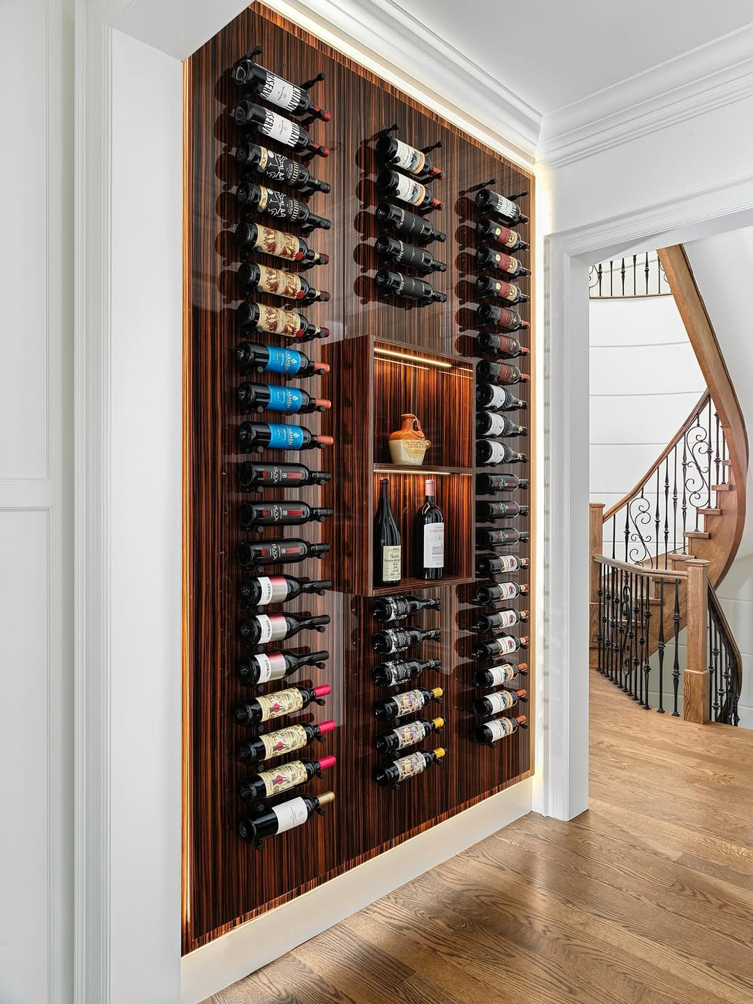 A built-in wine rack with horizontal bottle storage is mounted on a wood-paneled wall, featuring a central shelf holding wine bottles and a ceramic jug—an inspired touch for modern wine rack ideas in the hallway.