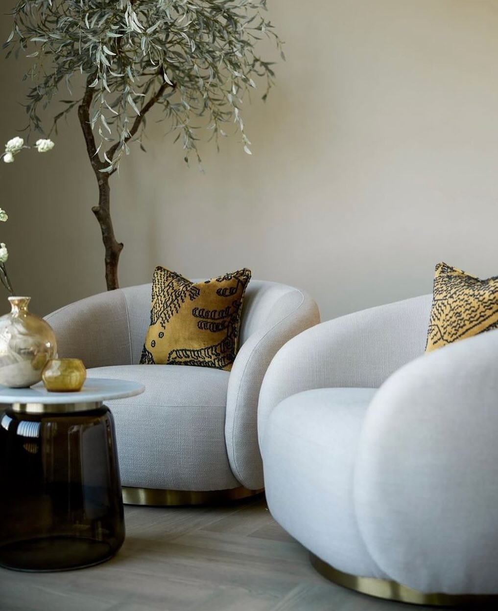 Two modern light gray armchairs with patterned yellow cushions sit beside a small round table and a leafy indoor plant, creating fresh inspiration for an organic modern living room.