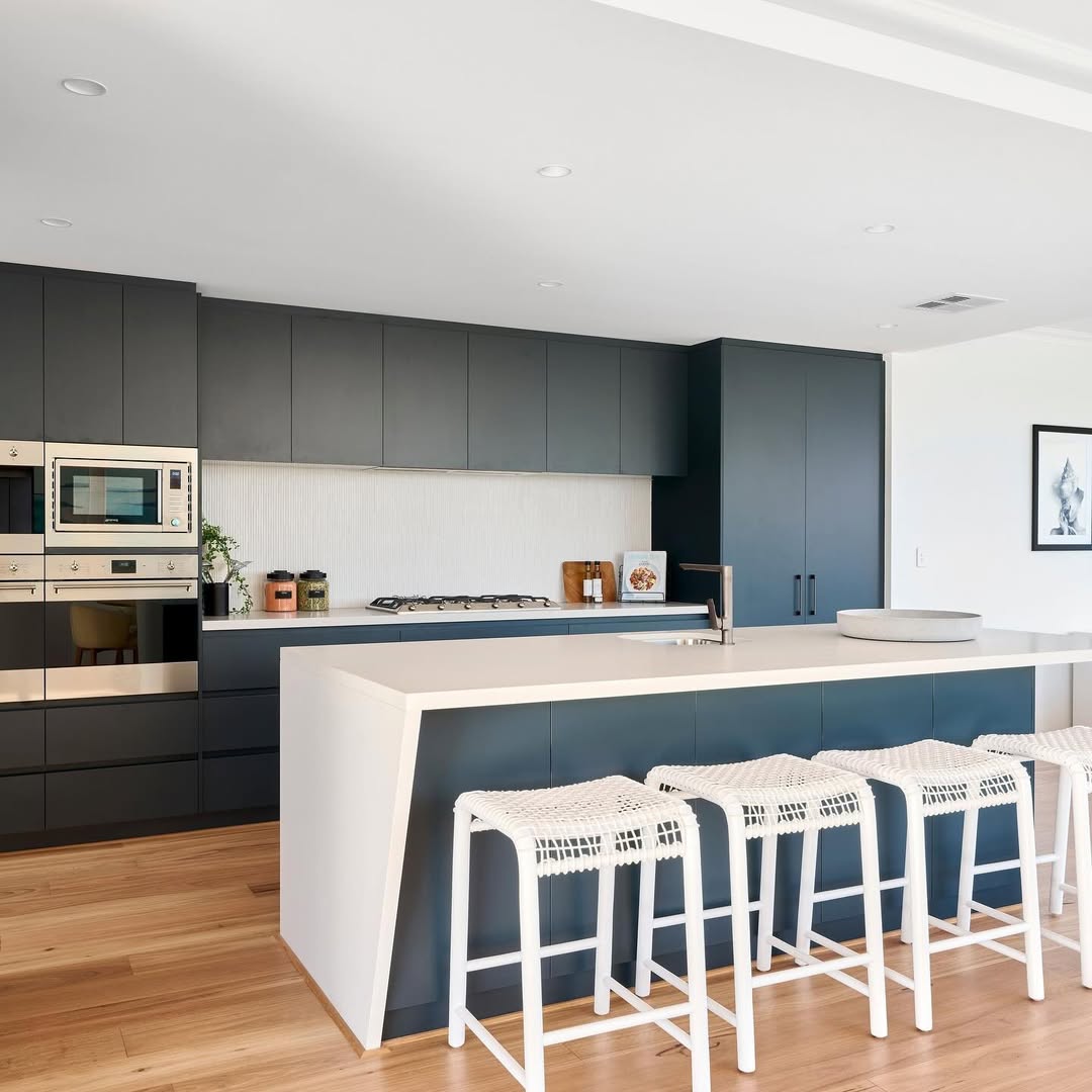 Modern kitchen with dark cabinets, built-in appliances, a white island countertop, and four white woven bar stools on a light wood floor—a perfect showcase for stunning kitchen colors and inspiring kitchen color ideas.