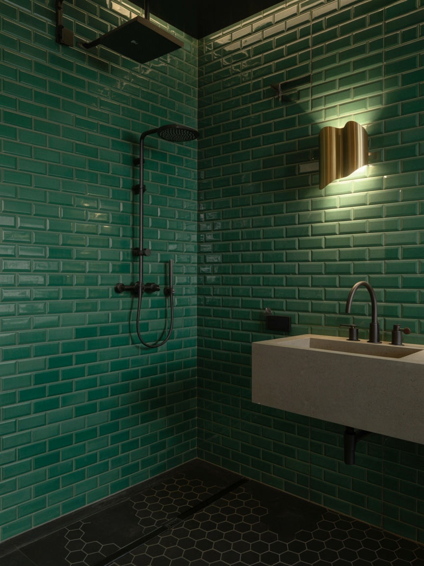 Modern, spa-worthy bathroom with green subway tile walls, dark fixtures, a square rainfall showerhead, wall-mounted sink, and a glowing wall light—perfect for inspiring your next bathroom design.