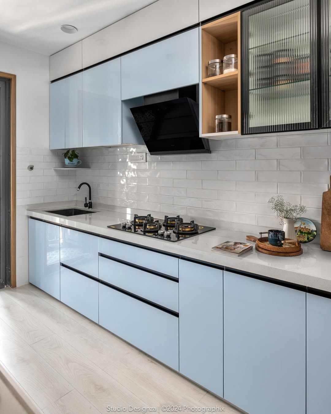 Modern kitchen with glossy light blue cabinets—one of the stunning kitchen colors for 2025—black appliances, white subway tile backsplash, and a countertop with stylish kitchen items and decor. Stay ahead in kitchen design trends!.