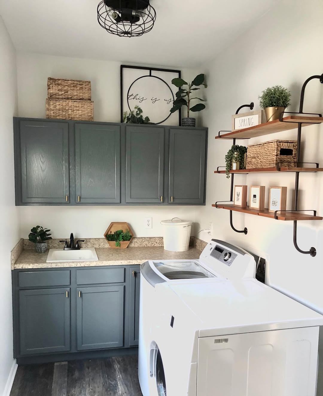 Boho laundry room with gray cabinets, a white washer, countertop with a sink, open shelves displaying boho laundry decor, and woven baskets for storage.