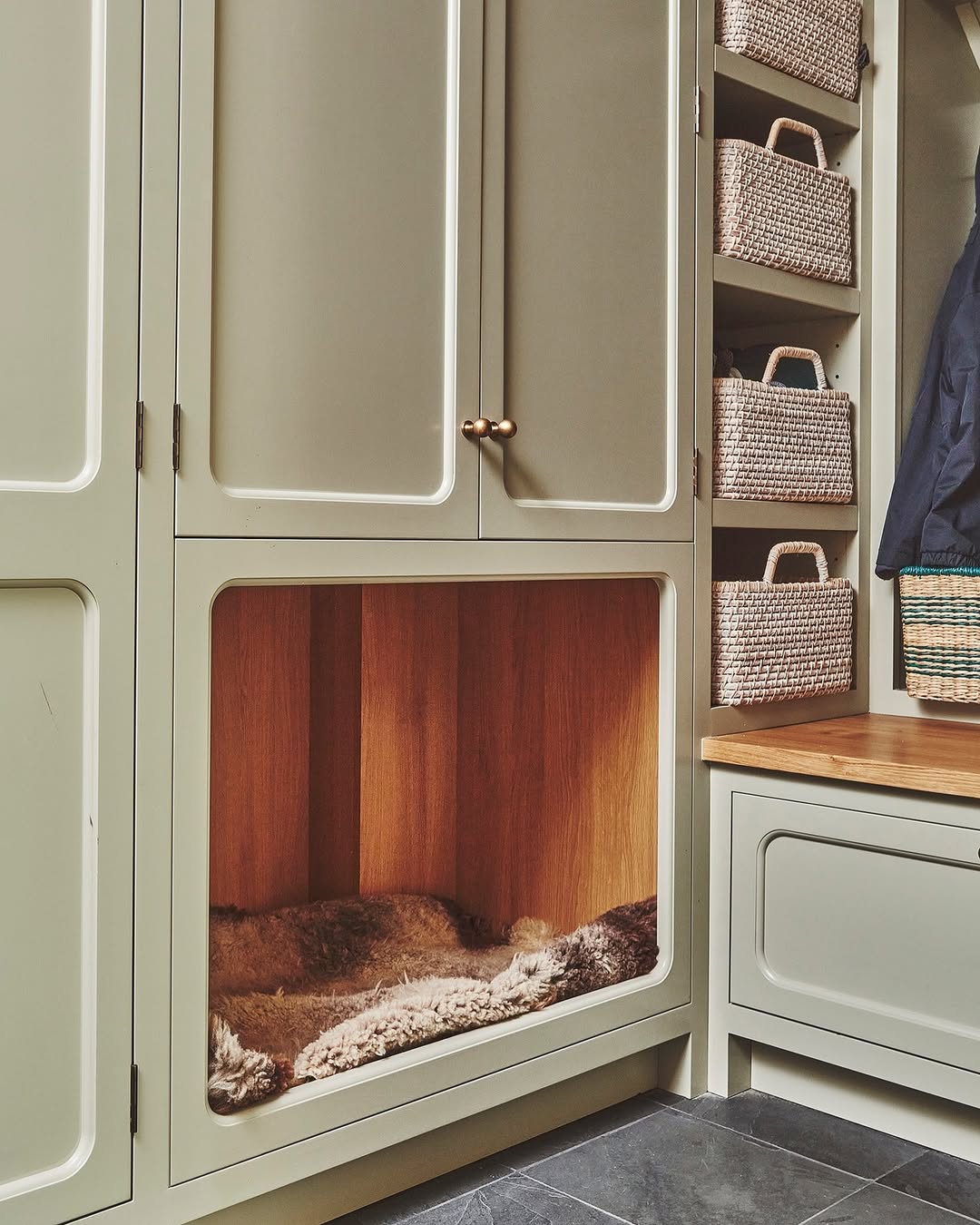 Built-in pet nook with a cushioned bed, next to a bench and shelves holding woven baskets, in a light-colored cabinetry setting—an inspiring touch for stylish Pet Bedroom Design.