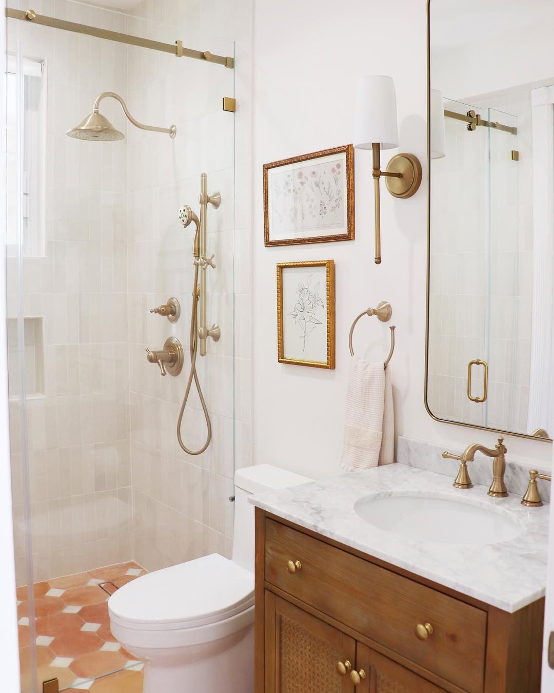 A spa-worthy bathroom featuring a glass shower, gold fixtures, marble countertop, wooden vanity, wall-mounted art, a towel ring, and a rectangular mirror offers inspiring bathroom tile ideas and stunning modern bathroom design.
