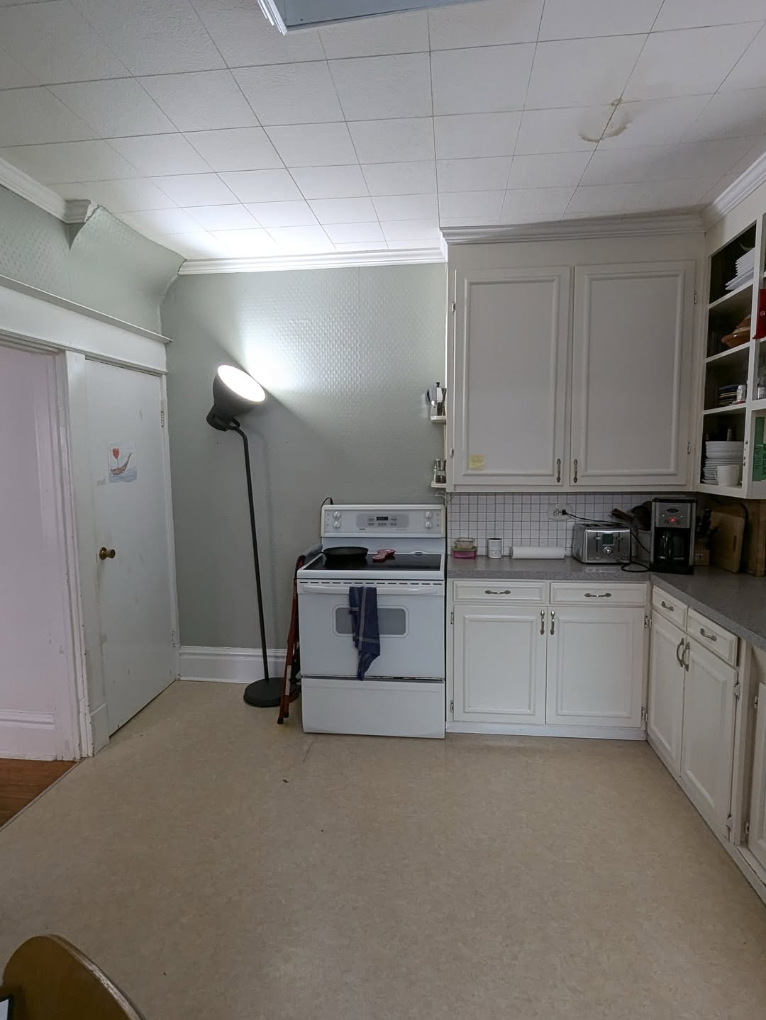 A kitchen with white cabinets, a white stove, a floor lamp in the corner, and various small appliances on the counter offers clever built-in storage solutions for effortless home organization.