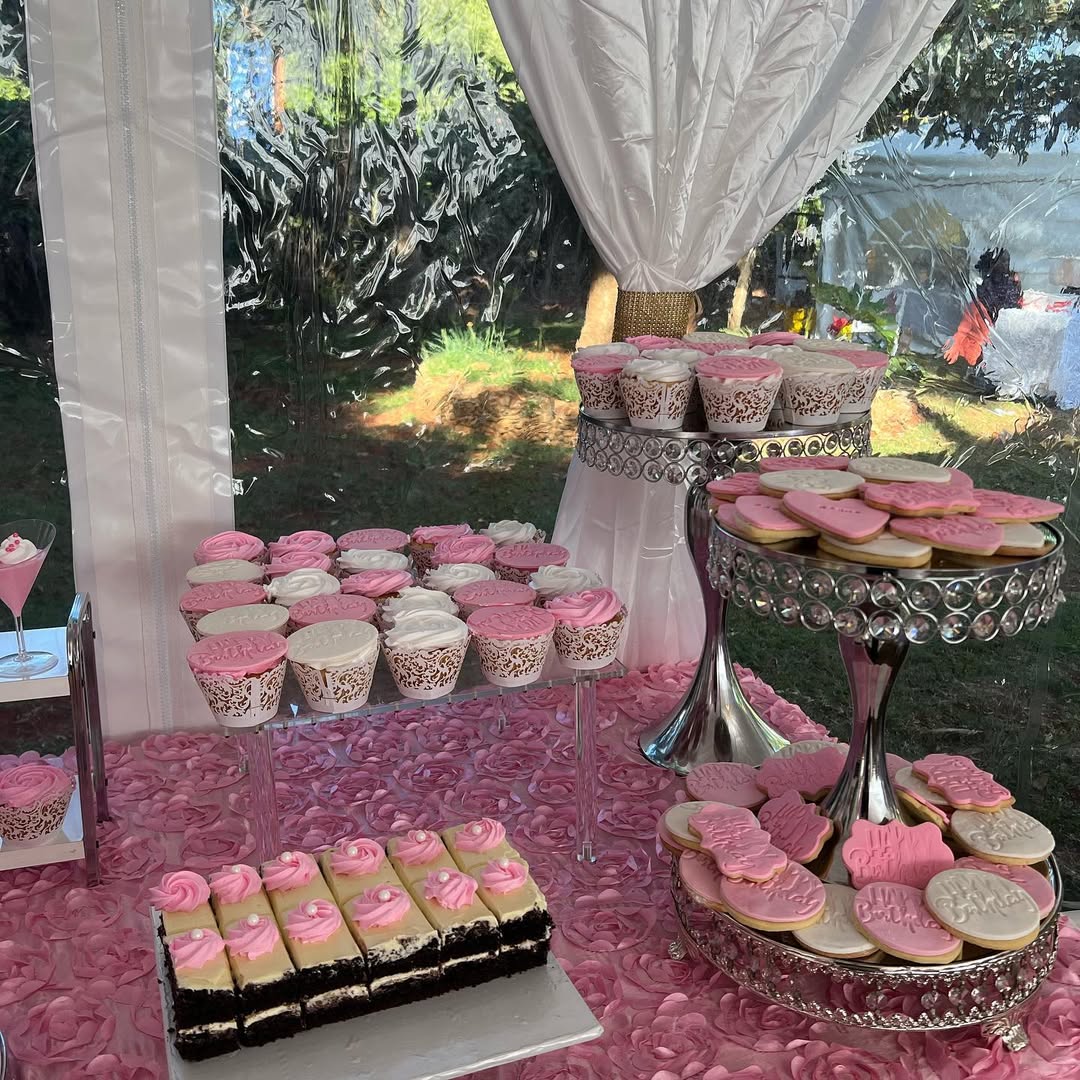 A dessert table with pink and white cupcakes, heart-shaped cookies, and layered cake slices arranged on stands atop a pink tablecloth under a white canopy—perfect for party desserts and inspiring dessert table ideas.