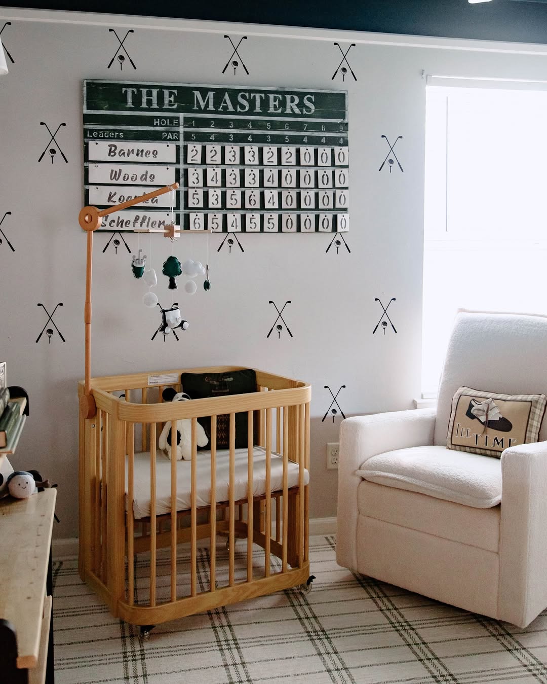 A chic nursery idea for a first-time mom, this baby boy nursery features a golf theme with a crib, plush chair, golf-themed decor, and a scoreboard wall display labeled