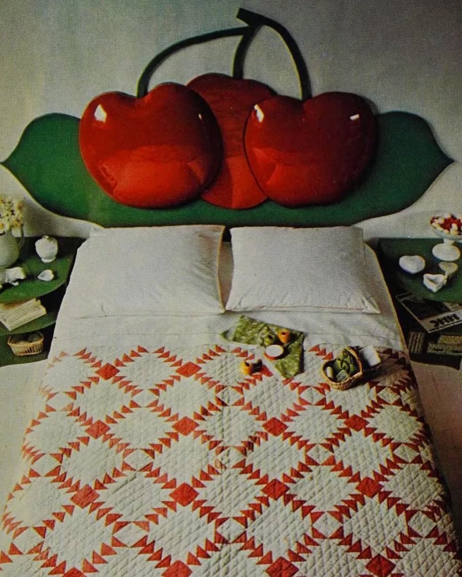 A bed with a red and white diamond quilt and a headboard shaped like two large red cherries with green leaves offers playful Cherry Bedroom Ideas; nightstands hold small items and books.