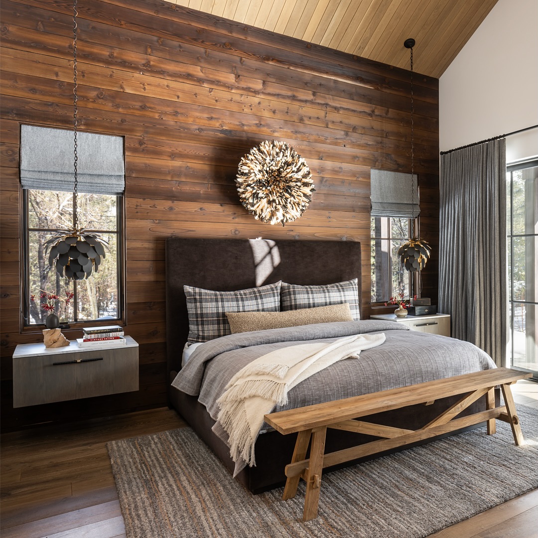 Modern rustic bedroom with a wooden accent wall, upholstered bed, plaid bedding, two pendant lamps, sunburst wall decor, floating nightstands, and a wooden bench—perfect for those seeking fresh bedroom ideas with rustic decor charm.
