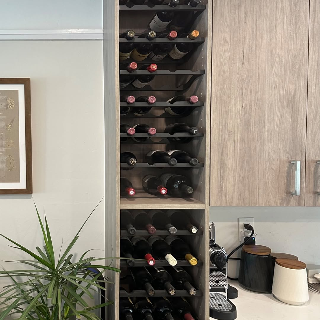A tall wooden wine rack offers stylish wine storage, filled with bottles beside a kitchen counter that holds a coffee machine, containers, and a potted plant.