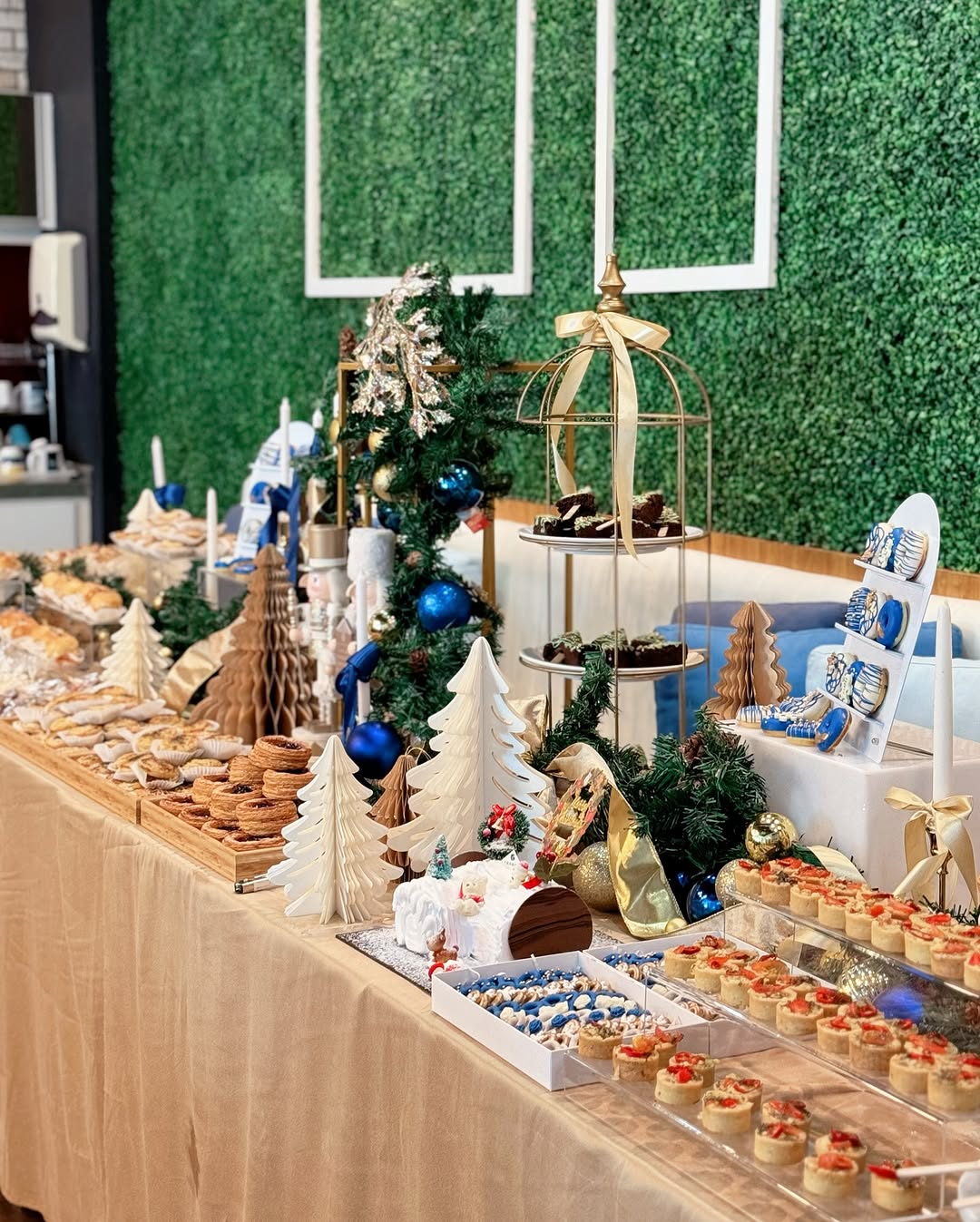 A dessert table decorated with Christmas trees, ornaments, and greenery, featuring pretty desserts and assorted pastries displayed on trays and stands—perfect for festive dessert table ideas.