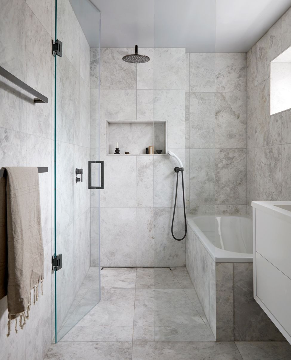 Modern bathroom with gray marble tiles, a glass shower enclosure, wall-mounted showerhead, built-in shelf, white bathtub, white vanity, and a beige towel on a rack—perfect inspiration for spa-worthy bathroom design.