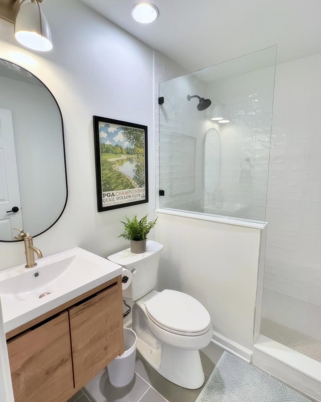 Modern Bougier Bathroom with a glass-enclosed shower, white walls, vanity with wood cabinet, wall mirror, framed artwork, potted plant on the toilet, and gray tile flooring that make the bathroom feel bigger.