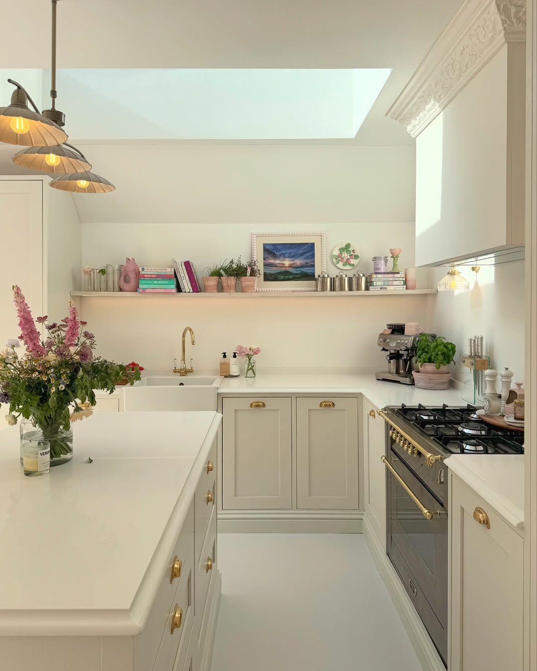 Bright, modern kitchen with white cabinets, brass hardware, a black stove, skylight, flowers on the island, open shelving, and cottagecore decor arranged neatly for charming kitchen ideas.
