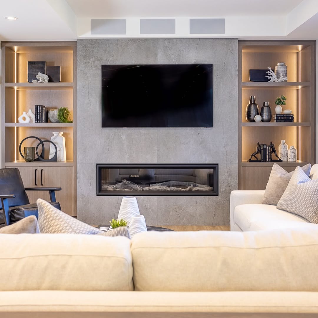 Modern built-in shelves living room featuring a wall-mounted TV above a linear fireplace, stylish decor, and neutral-colored sofas and accents.