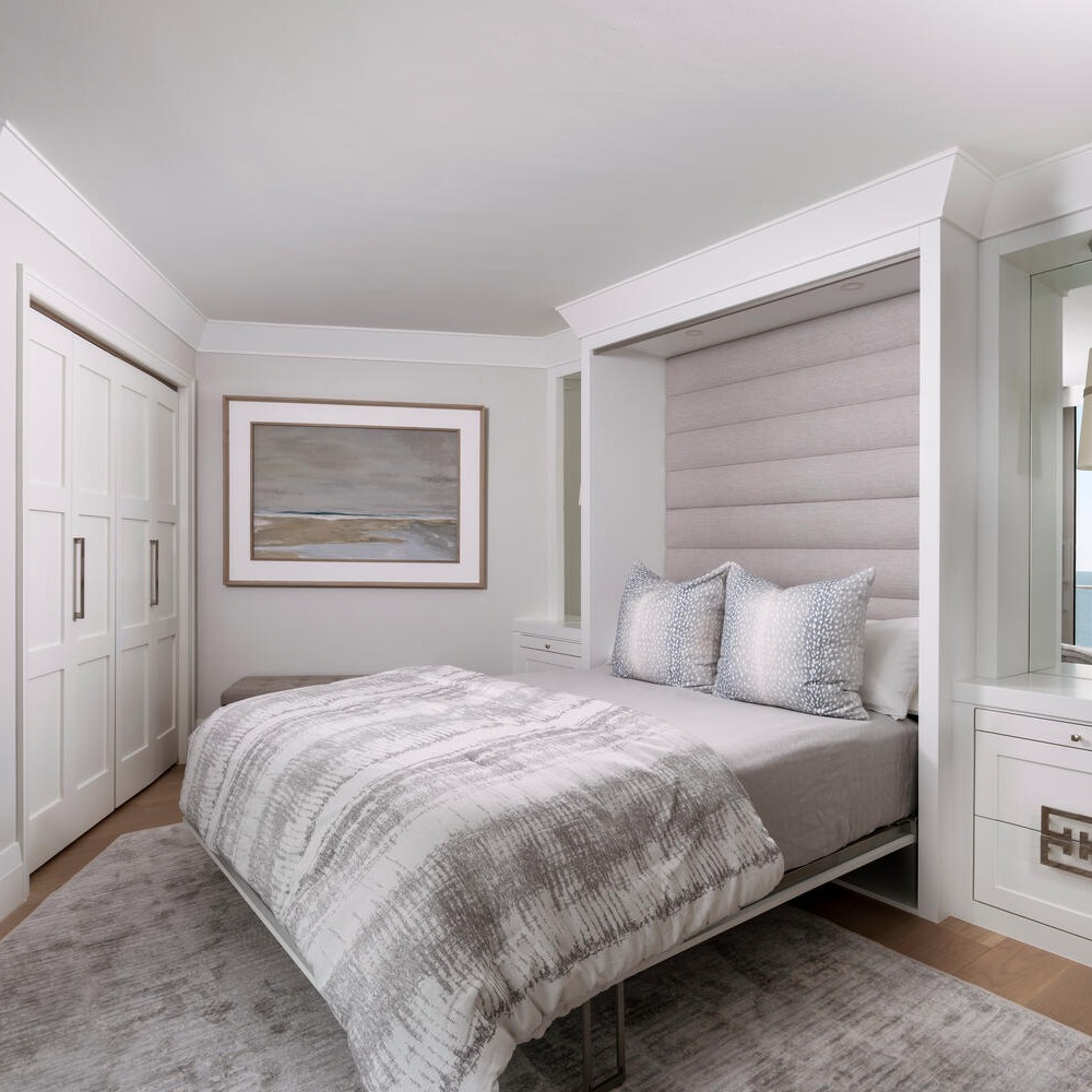 A modern bedroom featuring a pull-down Murphy bed, neutral bedding, built-in storage, a large rug, and a landscape painting—perfect for those seeking stylish Murphy Bed ideas in their space.