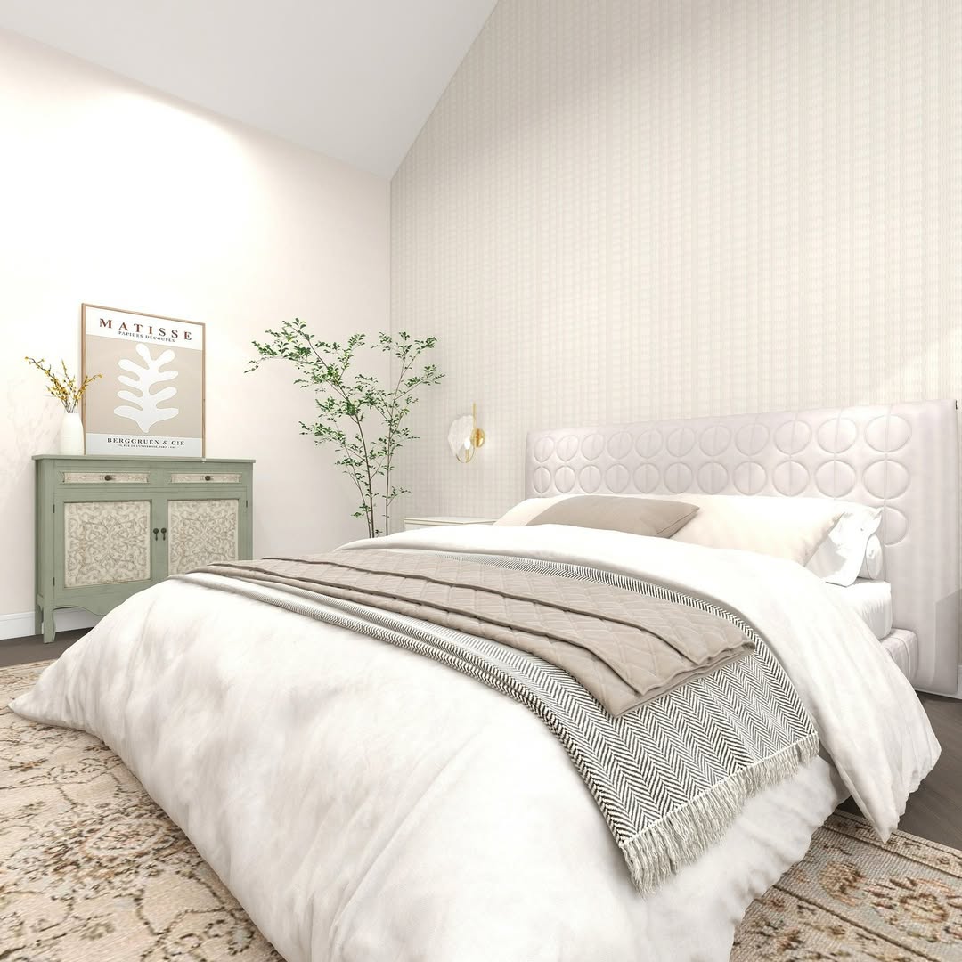 A modern bedroom with a white bed, beige and gray bedding, a patterned rug, green side cabinet, framed artwork, and a plant in the corner against light-colored walls—perfect for women bedroom ideas and fresh bedroom inspiration.