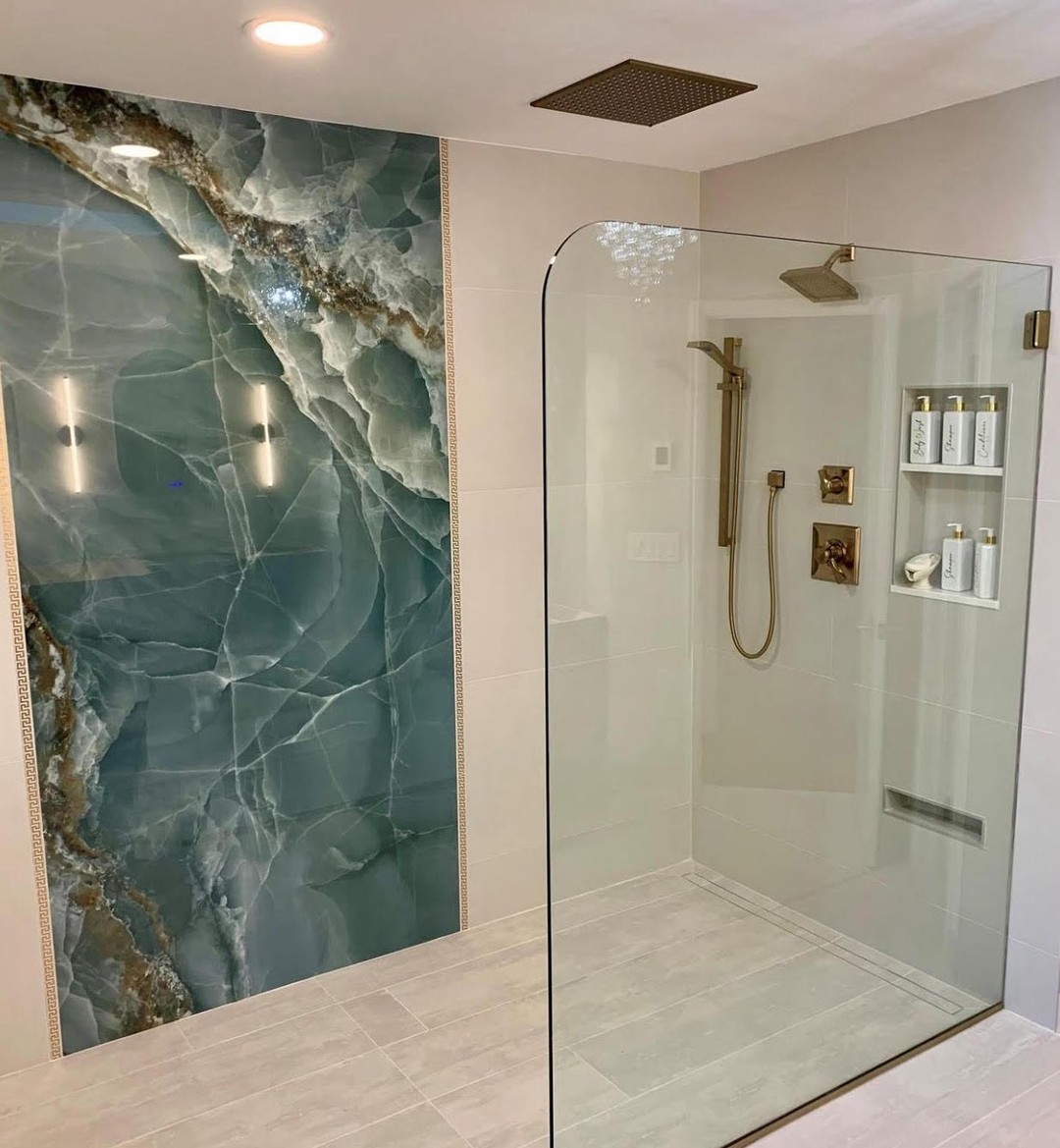 Modern spa bathroom with a large glass-enclosed shower, gold fixtures, built-in shelf for toiletries, and a feature wall with striking green and white veined marble—perfect inspiration for your next bathroom design.